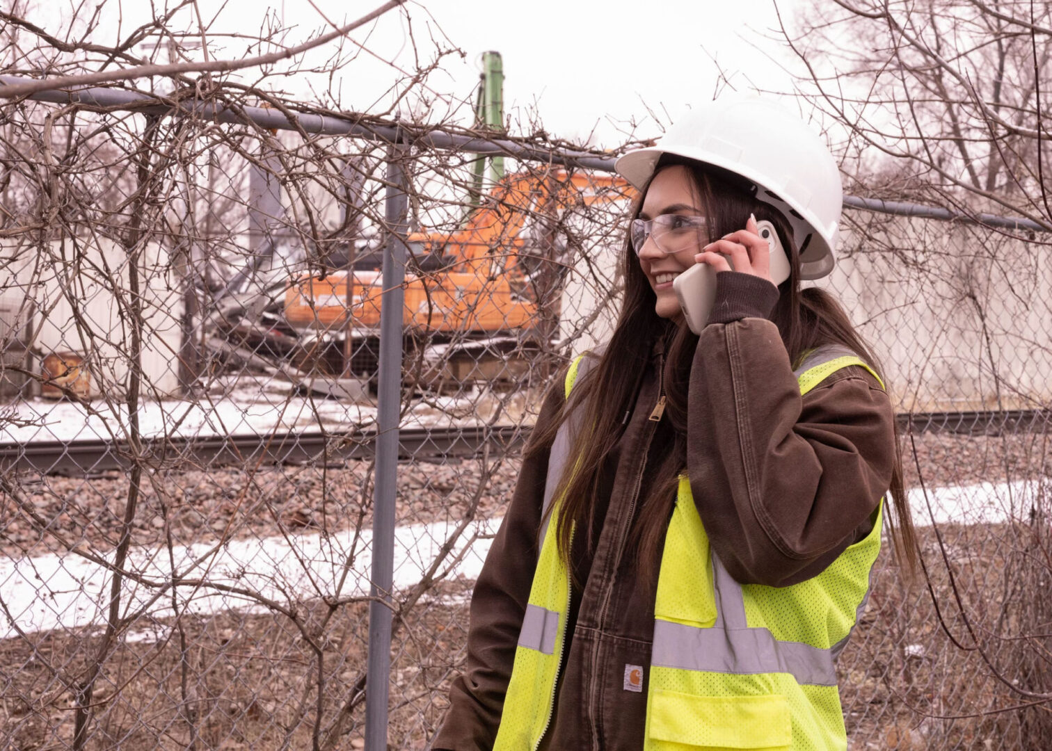 A woman in yellow vest and hard hat talking on cell phone.