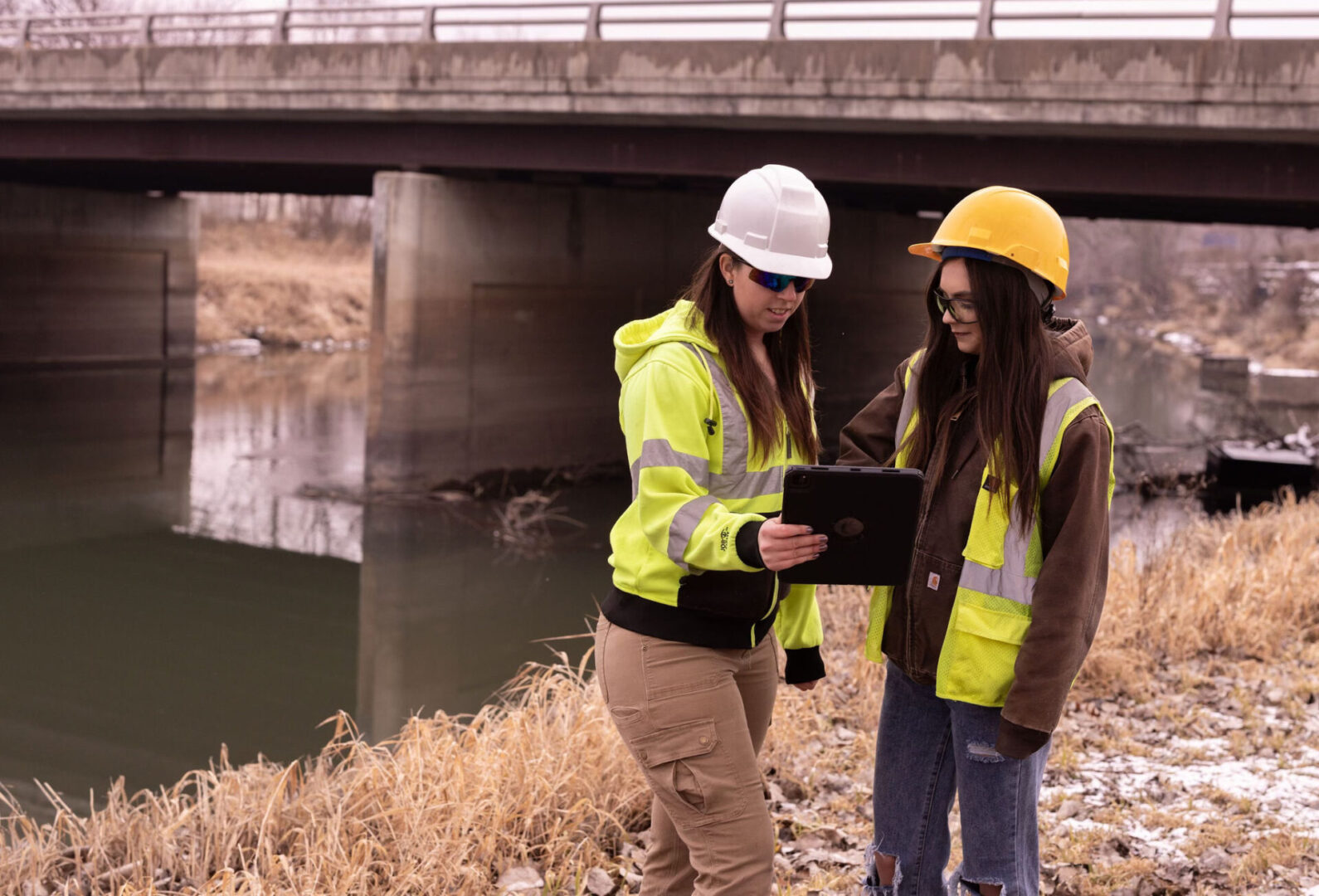 Two women in hard hats and jackets looking at a tablet.